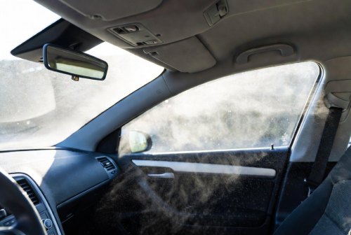 Zichtbaar fijnstof in een auto-interieur, met stofdeeltjes in het zonlicht bij het zijraam, dashboard en achteruitkijkspiegel.