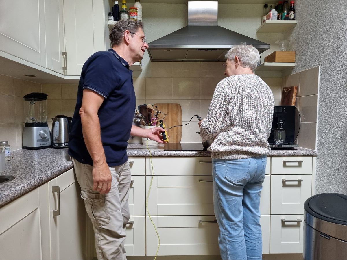 Woonbioloog Erik Leemkuil meet in de keuken met een handmeter, terwijl een klant bij het fornuis staat.