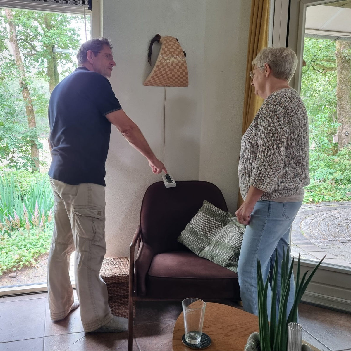 Woonbioloog Erik Leemkuil meet in een woonkamer met een handmeter, terwijl een klant toekijkt.