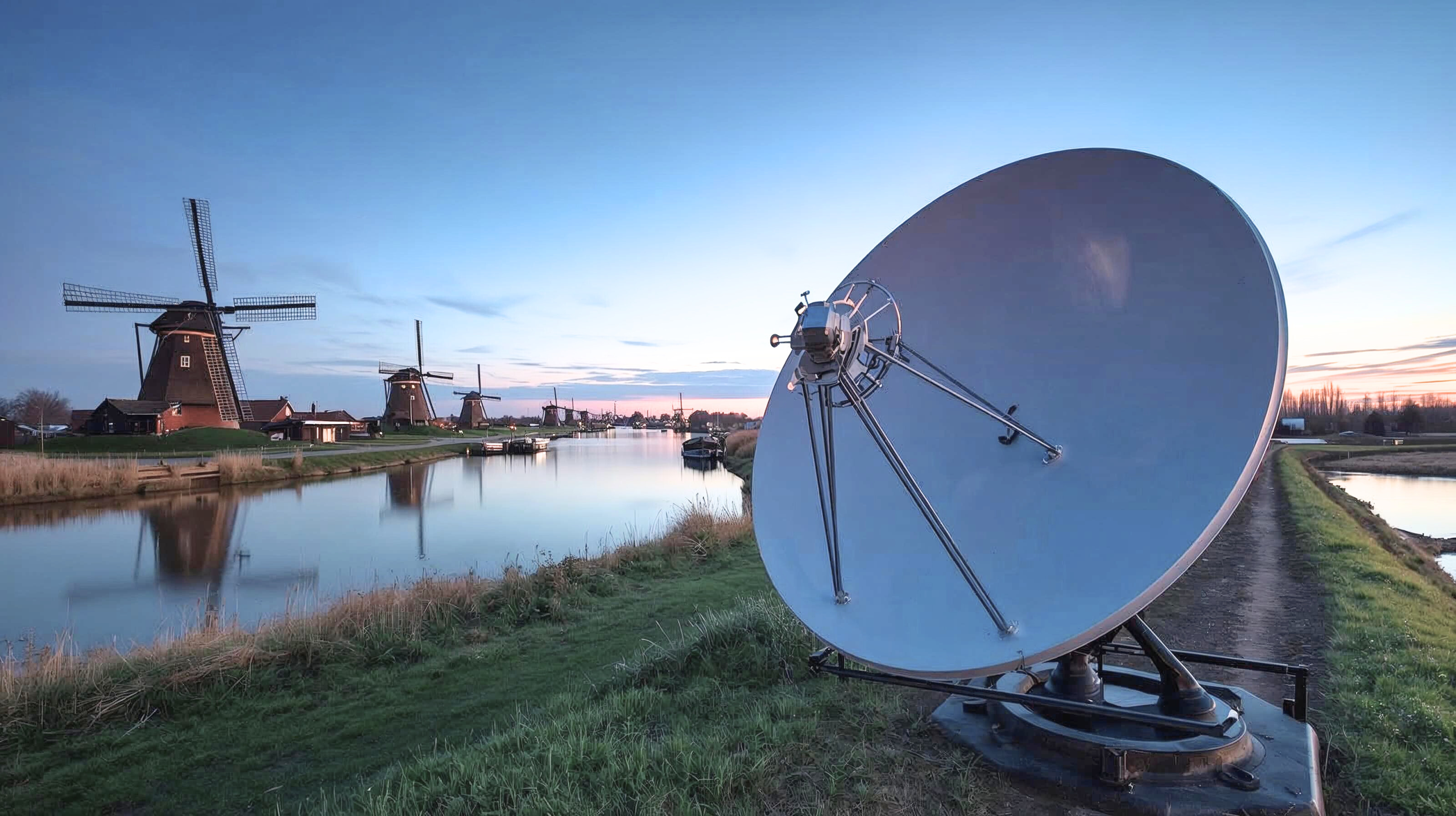Grote schotel naast Hollandse molens bij zonsondergang, als beeld bij satellietinternet in Nederland
