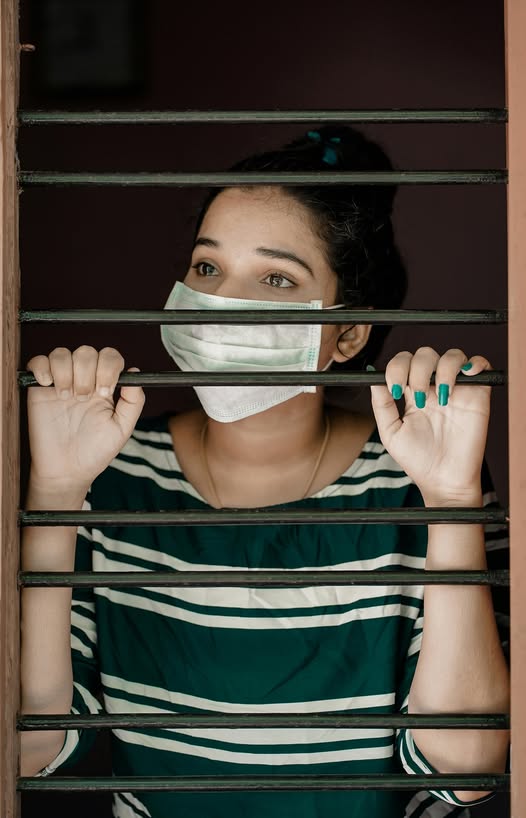 Vrouw met mondkapje kijkt angstig door tralies, als beeld van angst en onrust