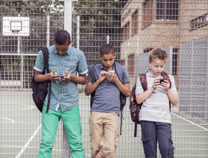 Drie jongens op een schoolplein kijken alle drie naar hun smartphone
