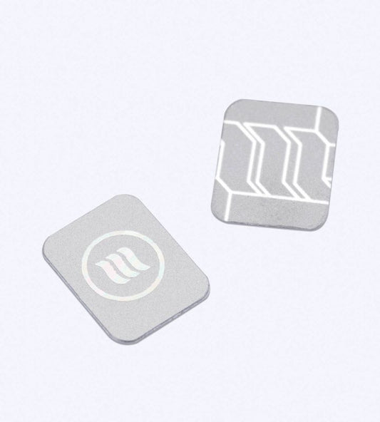 Twee zilverkleurige memonizerWIRELESS-stickers: één met memon-logo en één met patroon, op een lichte achtergrond.